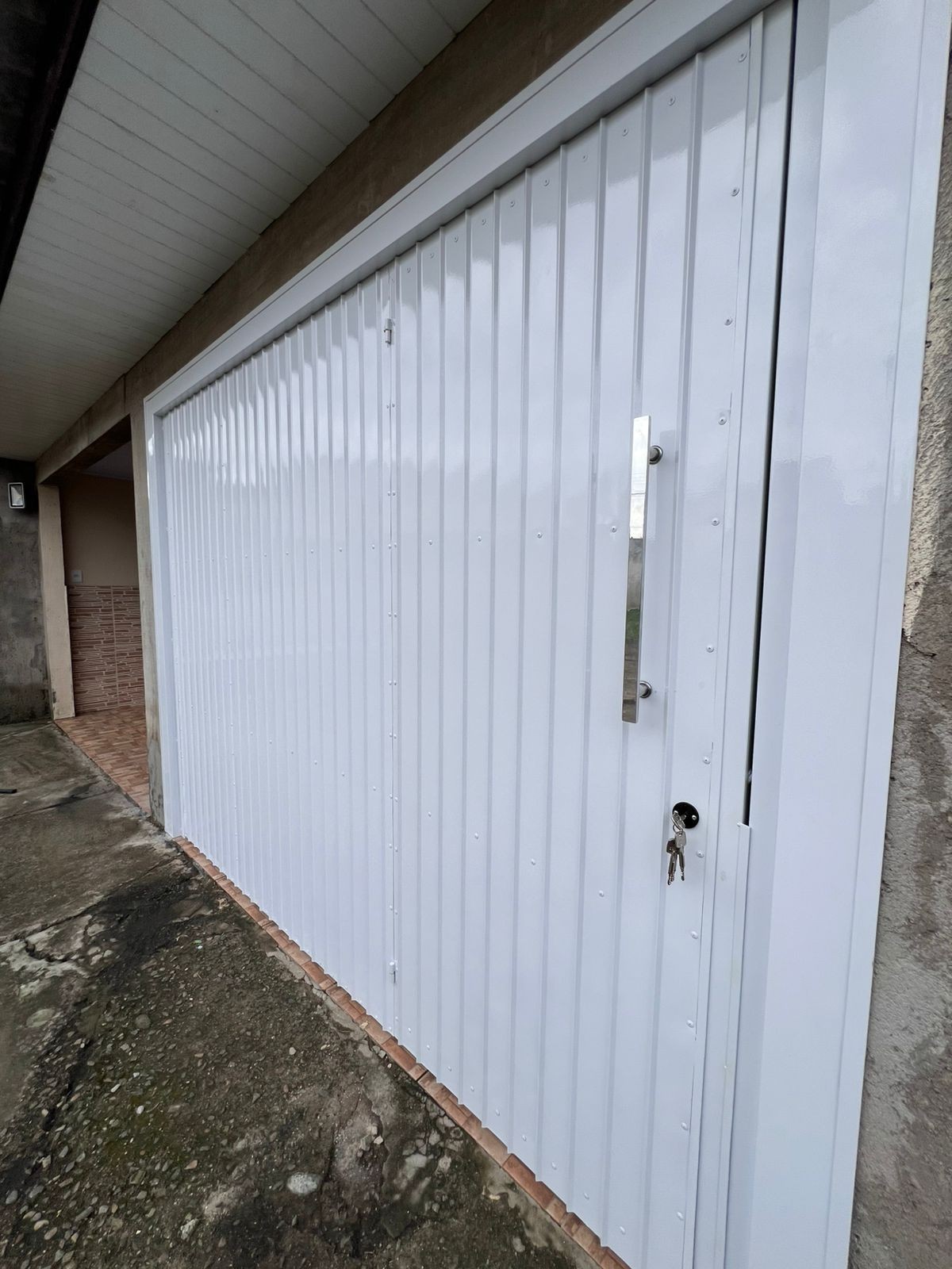 White metal garage door with vertical panels, key inserted in the lock, and a concrete driveway.
